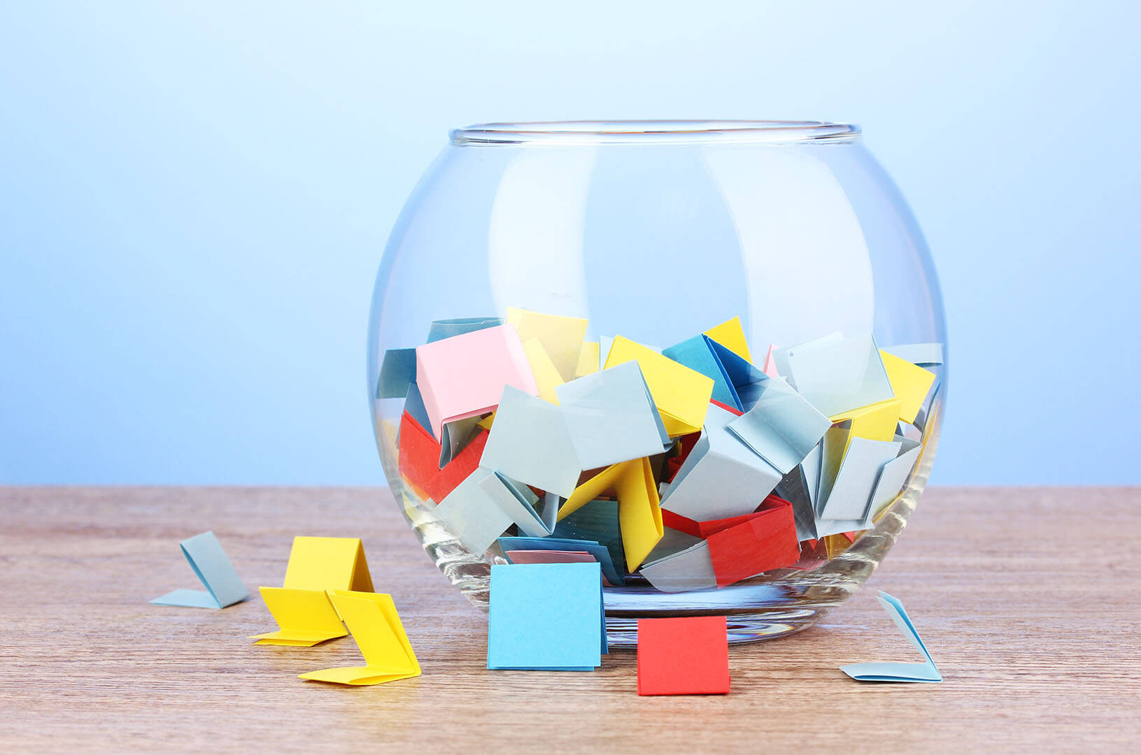 A fishbowl of brightly colored folded squares of paper represent with some scattered on the tabletop represents random QA sampling